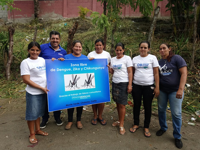 Monte Verde volunteers with a sign declaring Monte Verde to be a dengue, Zika, and chikungunya free zone.